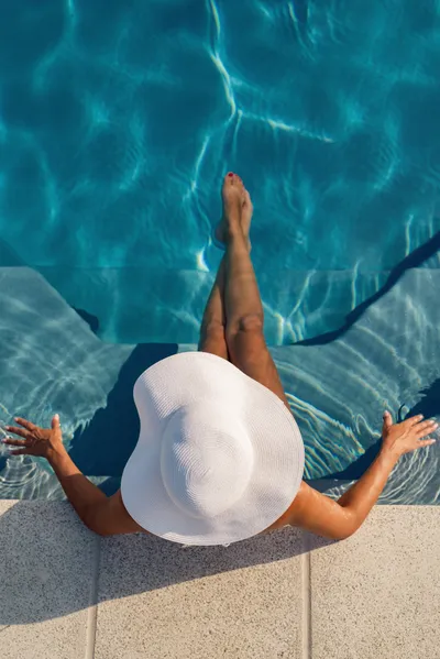 Tanned woman with bright hat sits relaxed in the pool