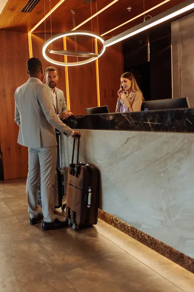 New hotel guests talking with young woman working as hotel receptionist